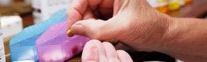 Hands sorting medications into a weekly pill holder with prescription drug bottles on table