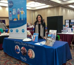 A woman stands between an expo table with marketing materials on it