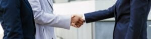 Three business women standing together as two are shaking hands.